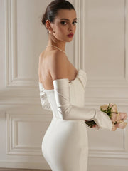 Woman in a white wedding dress holding flowers against a neutral wall.