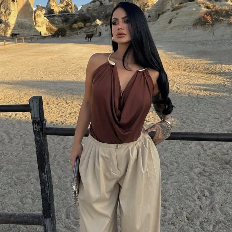 Woman in a brown top and beige pants standing in a desert-like landscape with rock formations.