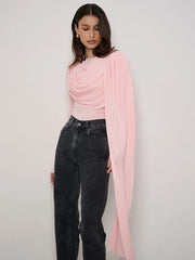 Woman wearing a pink top and black jeans with a light pink scarf on a white background
