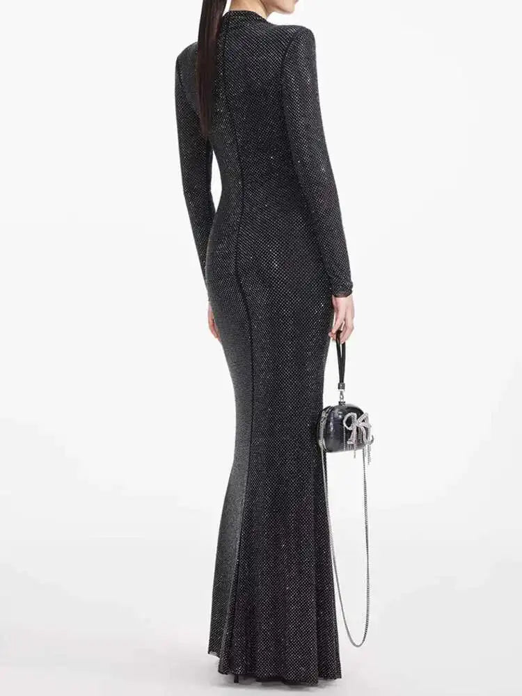 Woman wearing a long black dress holding a matching handbag on a white background