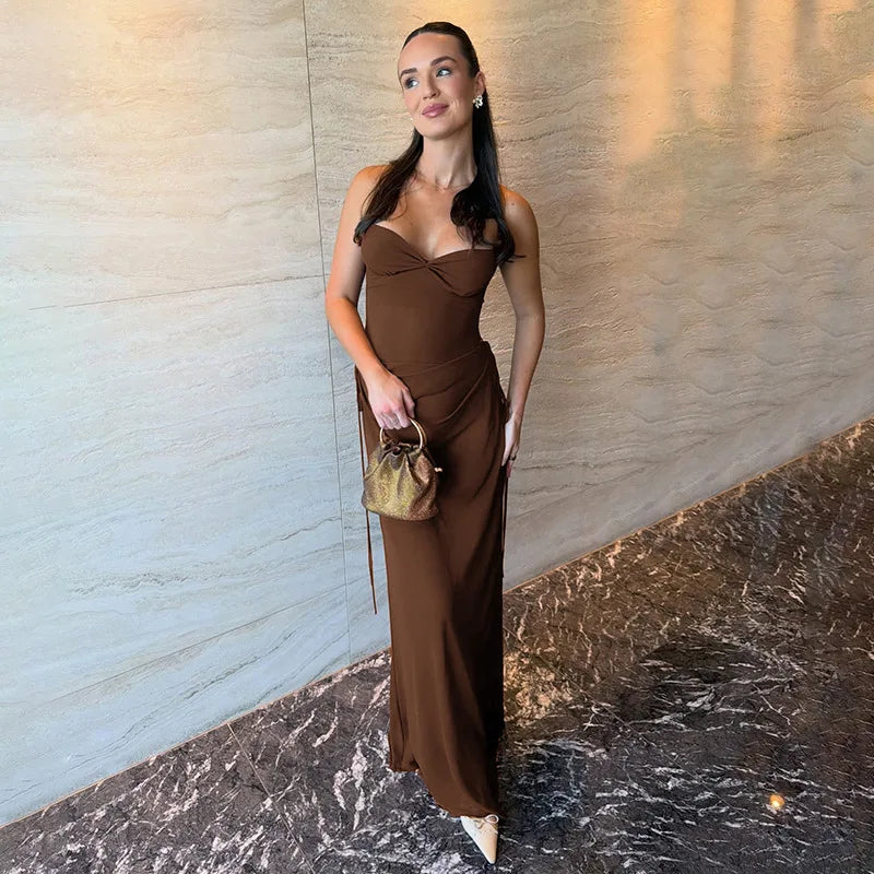 Woman in a brown dress holding a gold handbag against a marble wall.
