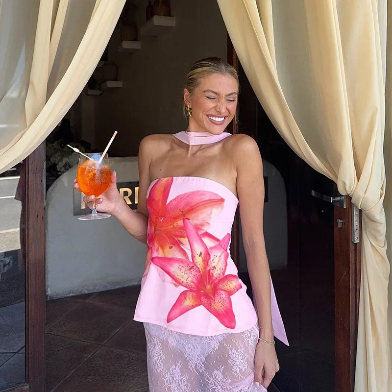 Woman in a floral dress holding a cocktail, standing in front of a building entrance.