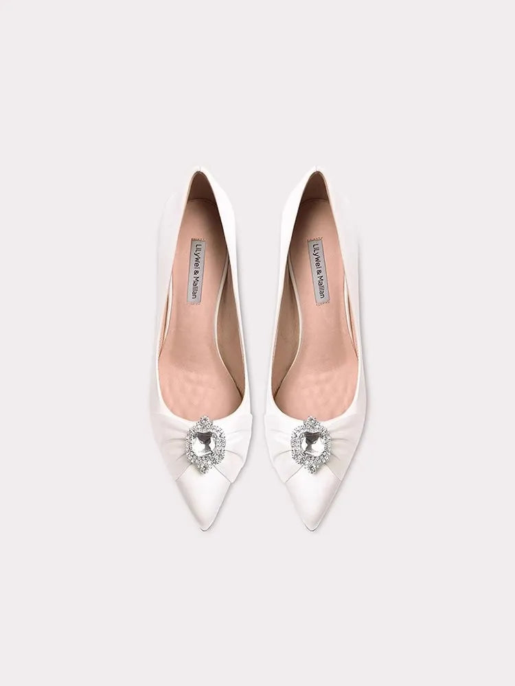 White pointed-toe shoes with crystal embellishments on a white background