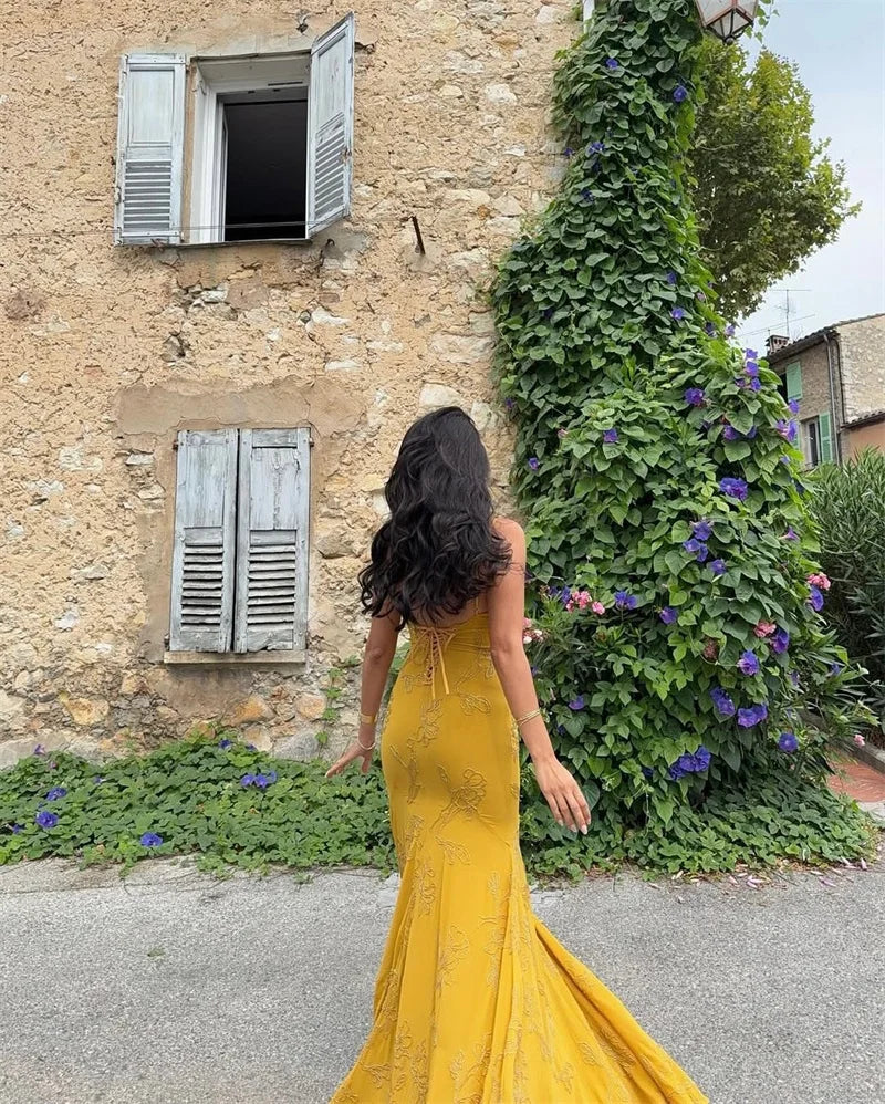 Woman in a yellow dress standing in front of a stone building with greenery.