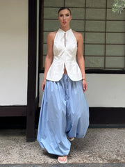 Woman wearing a white sleeveless top and light blue skirt standing in front of a traditional Japanese building.