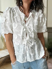 Woman wearing a white lace blouse with short sleeves and blue jeans indoors.