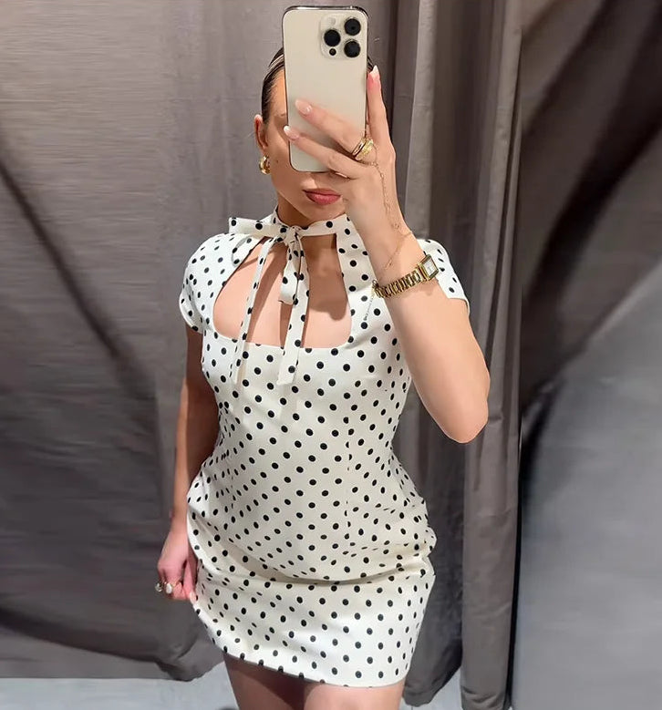 Person wearing a polka dot dress taking a mirror selfie against a plain background
