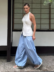 Woman wearing a white sleeveless top and light blue pants standing in front of a traditional Japanese sliding door.