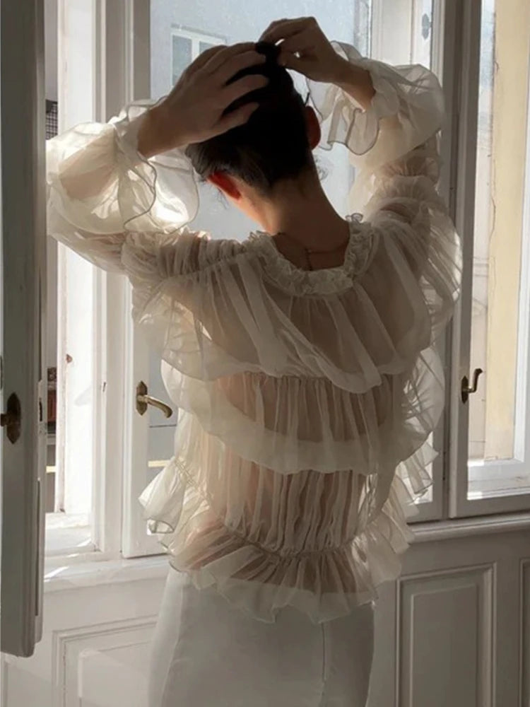 Person wearing a white blouse with ruffled sleeves in a bright room.