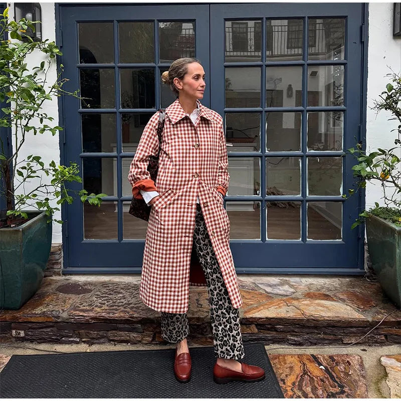 Woman in a checkered coat standing in front of a blue door with glass panels.