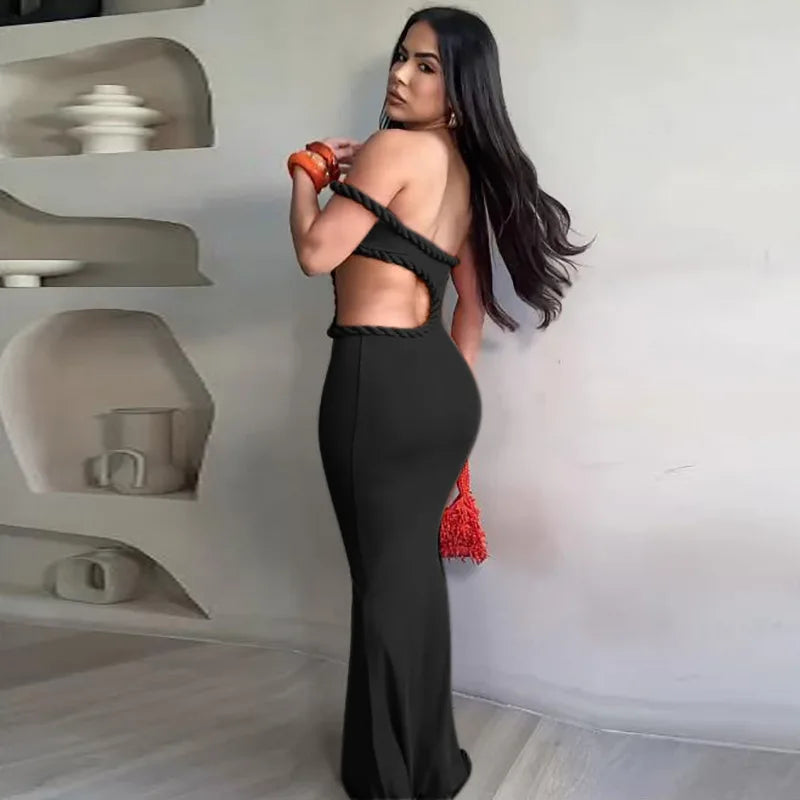 Woman in a black dress with red accents standing against a white wall.