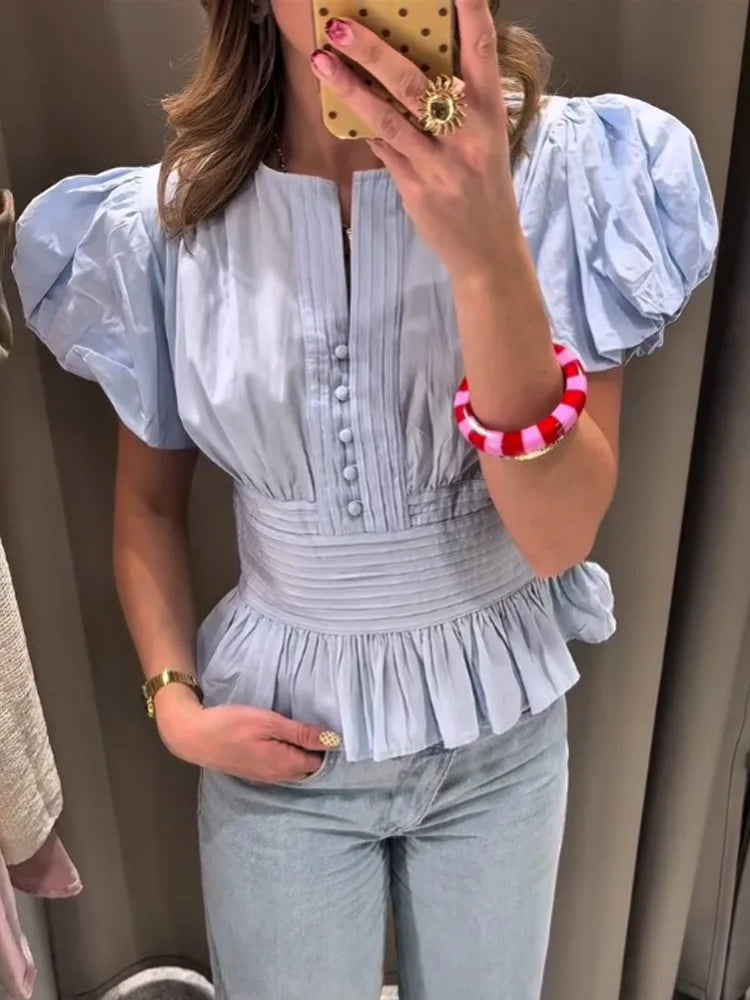 Person wearing a light blue top with puffed sleeves and jeans, taking a mirror selfie.