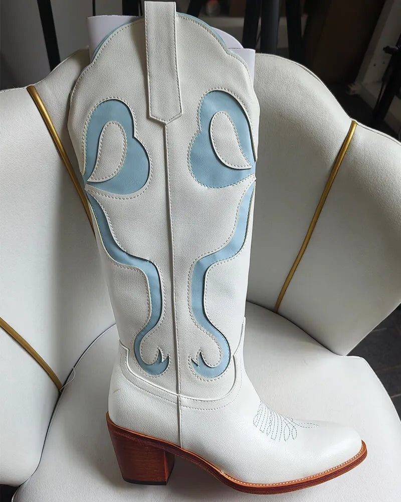 White cowboy boot with blue stitching on a white chair.