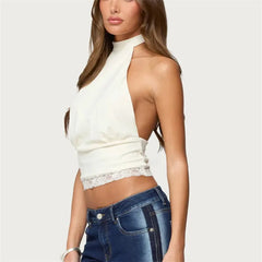 Woman wearing a white halter top with lace details and blue jeans on a plain background