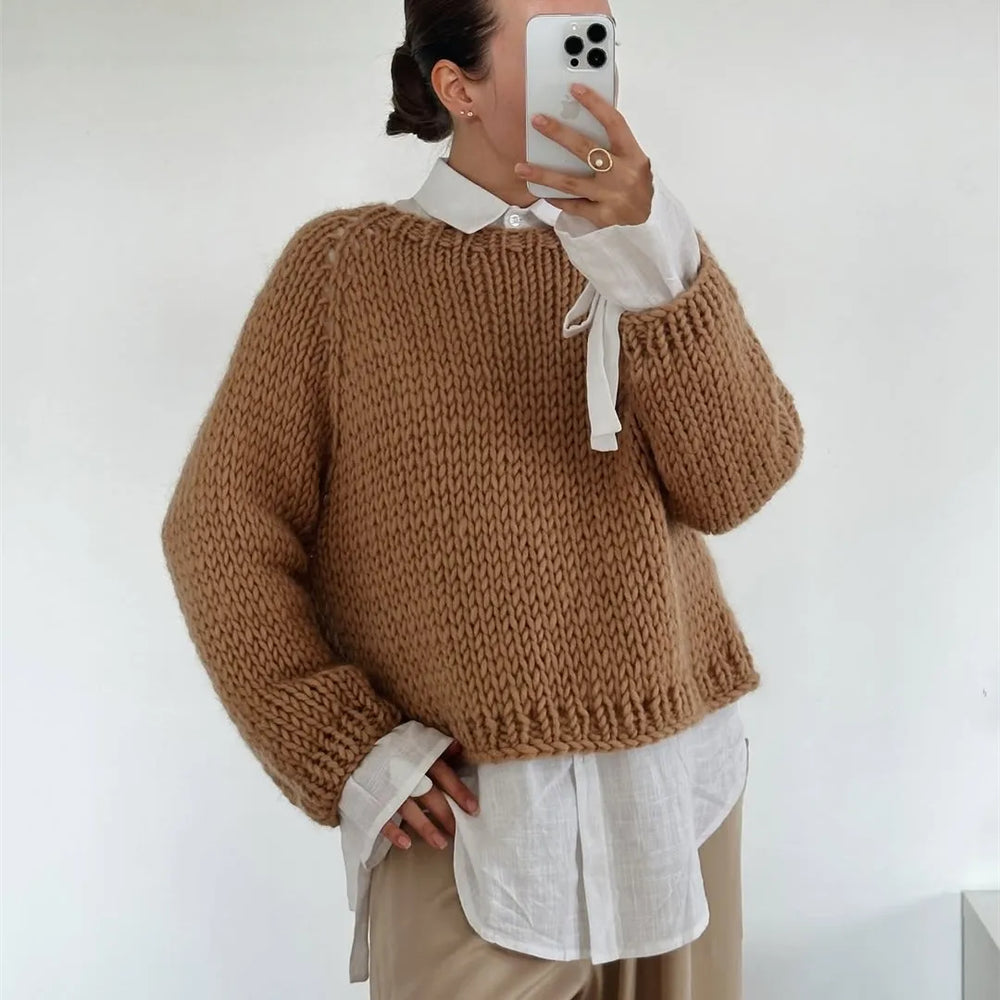 Person wearing a brown knitted sweater over a white shirt with a plain background