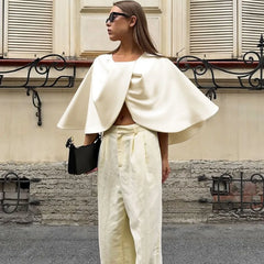 Woman wearing a white cape and pants standing in front of a building.