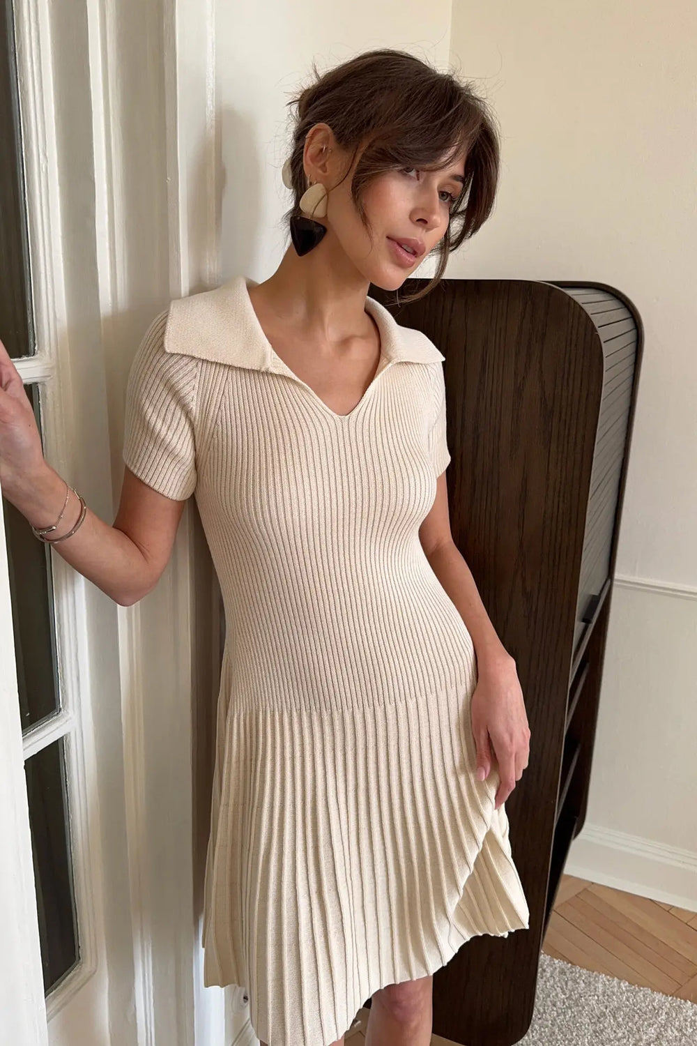 Woman wearing a beige pleated dress standing indoors.