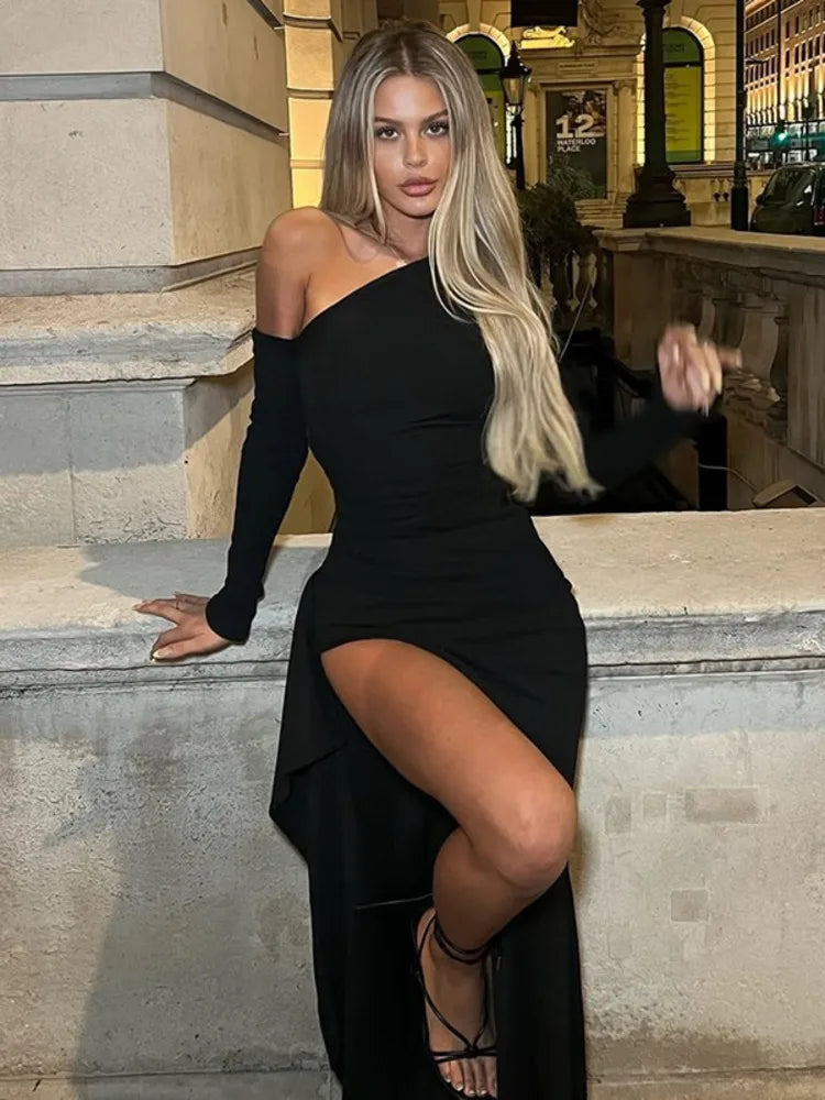 Woman in a black one-shoulder dress with a high slit standing on stone steps.