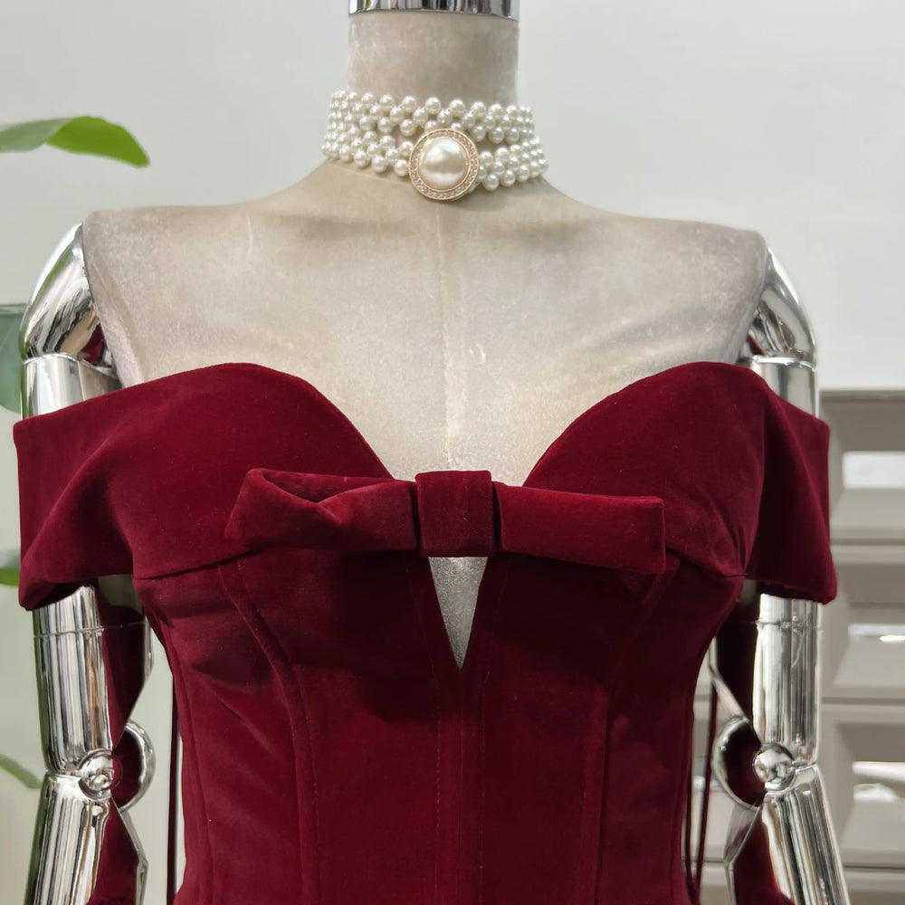 Mannequin wearing a burgundy dress with a large bow and pearl necklace on a white background