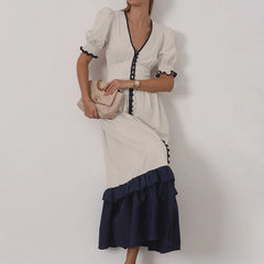 Woman wearing a white dress with navy accents against a plain background