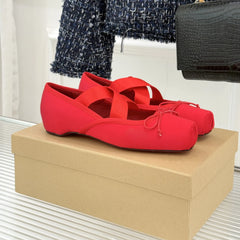 Red ballet flats on a beige shoe box with a black handbag and blue textured fabric in the background.