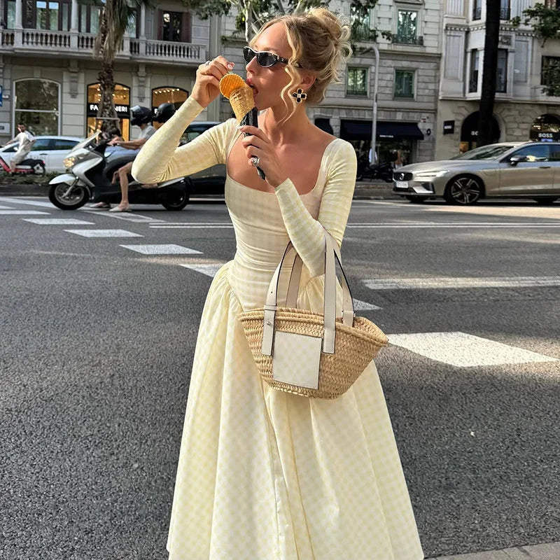 Woman in a light yellow dress with a straw bag crossing a street.