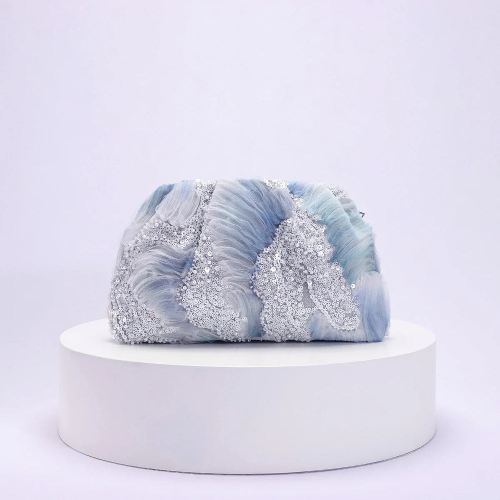 Blue and white marbled clutch with glittery accents on a white platform against a light purple background