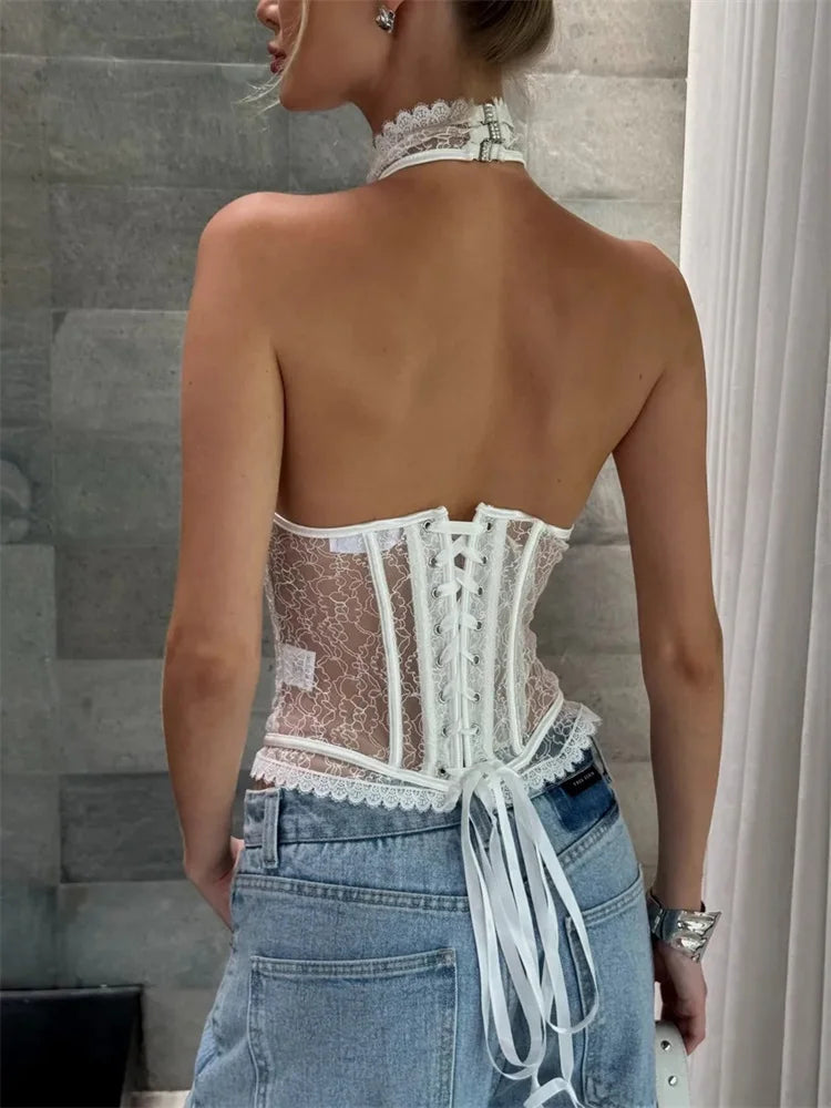 Person wearing a lace-up back top with sheer details and high-waisted jeans against a neutral background.