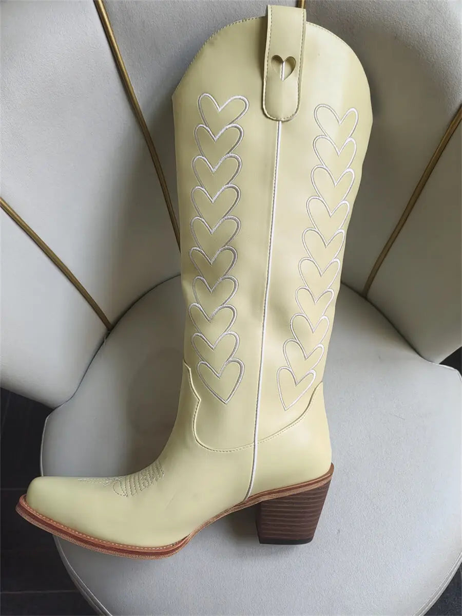 Light yellow cowboy boot with heart designs on a white surface