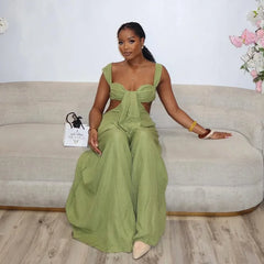 A woman in a green jumpsuit is sitting on a beige couch with a white wall and floral decorations in the background.