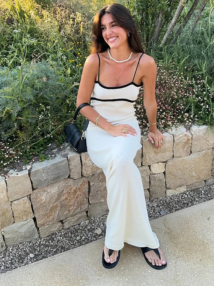 Woman in a white dress with black straps sitting on a stone wall outdoors.