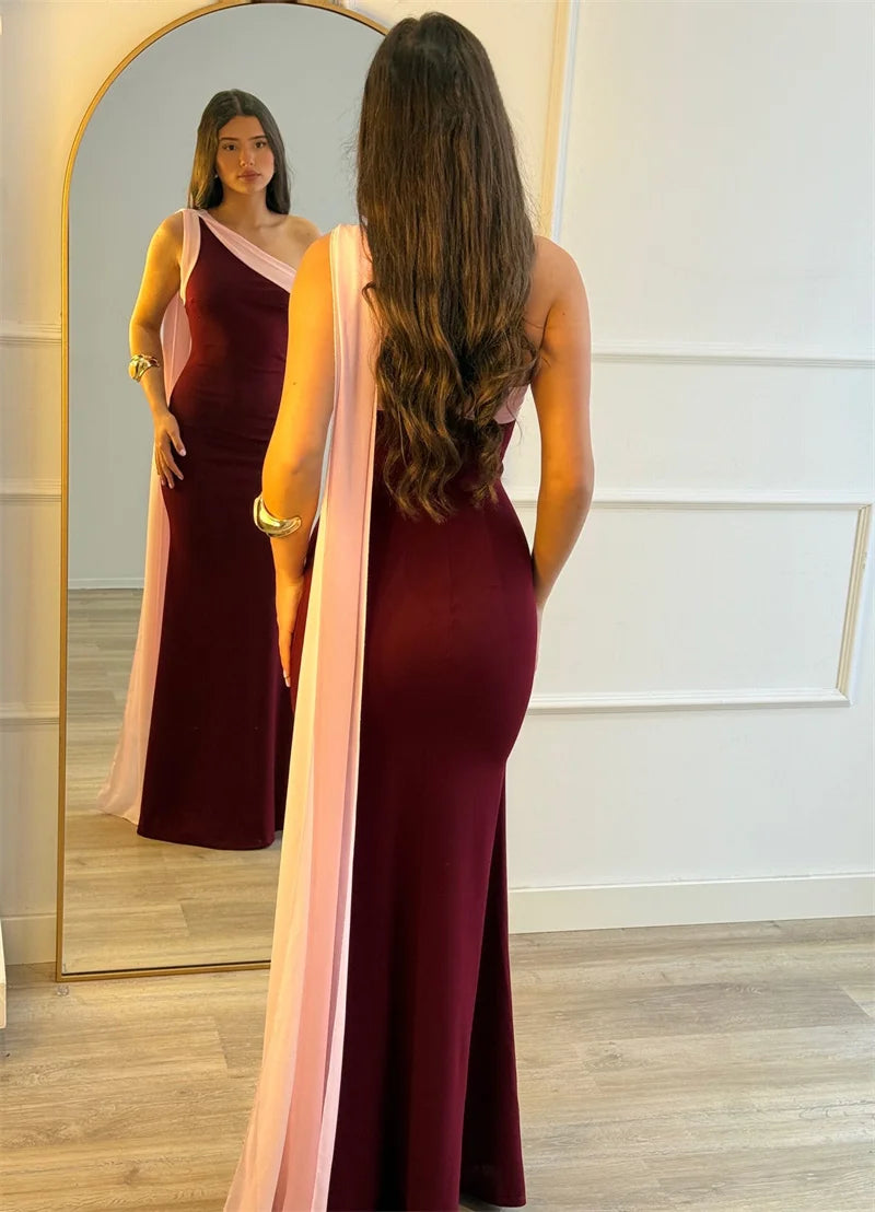 Woman in a burgundy evening gown with a pink overlay standing in front of a mirror.