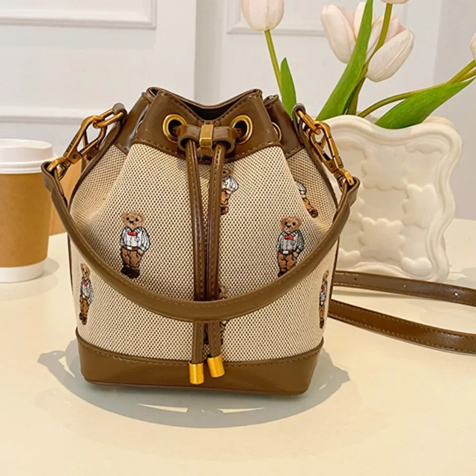 Bear print canvas bucket bag with brown faux leather trim and gold hardware.