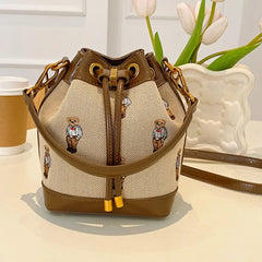 Bear print canvas bucket bag with brown faux leather trim and gold hardware.