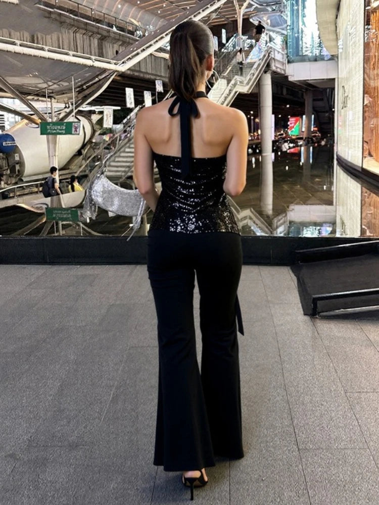 Person wearing a black sequined top and black flared pants in an indoor setting.