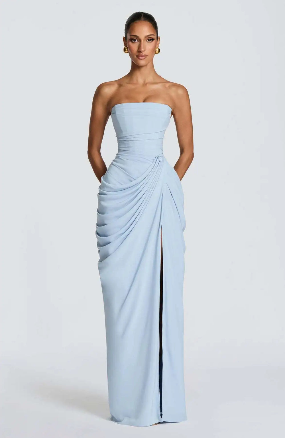 Woman wearing a light blue strapless gown with a slit on a white background