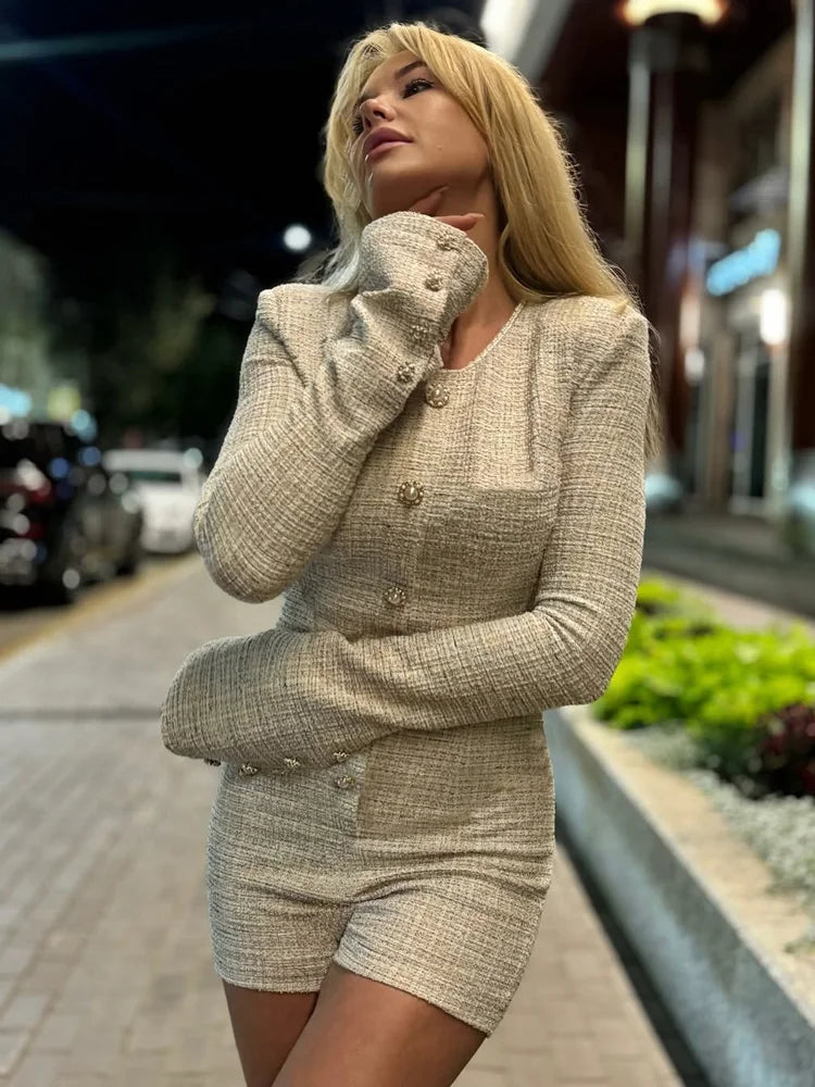 Woman in a tweed outfit standing on a sidewalk at night.