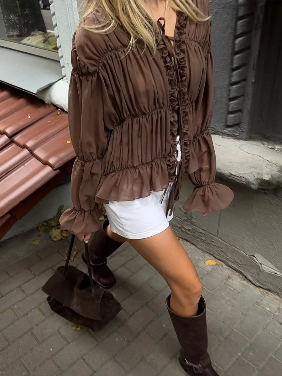 Woman wearing a brown ruffled blouse and white shorts on a sidewalk.