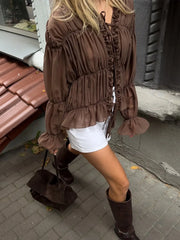 Woman wearing a brown ruffled blouse and white shorts on a sidewalk.