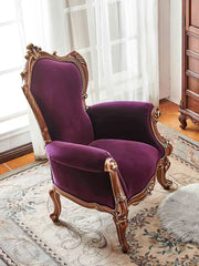 Purple armchair with gold accents in a room with white curtains and wooden floor.