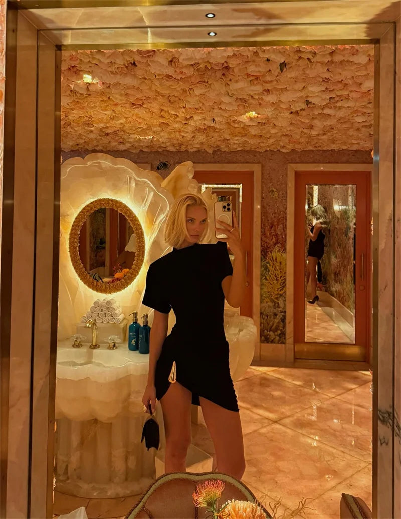 Woman in a black dress standing in a luxurious bathroom with marble walls and a large mirror.