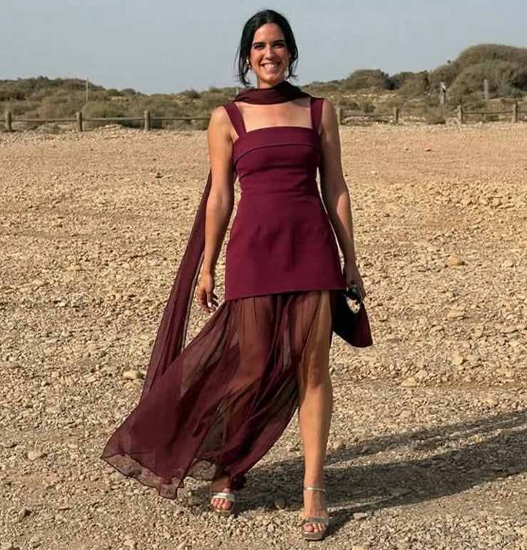 Woman in a burgundy dress standing in an open field with a clear sky.
