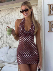 Woman in a polka dot dress holding a drink, standing against a textured wall.