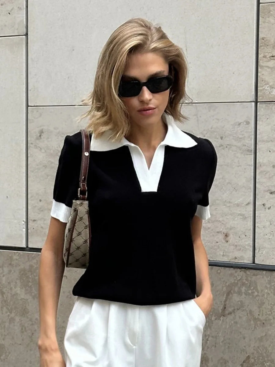 Woman wearing a black and white outfit with sunglasses against a gray tiled wall.