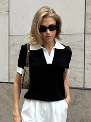 Woman wearing a black and white outfit with sunglasses against a gray tiled wall.