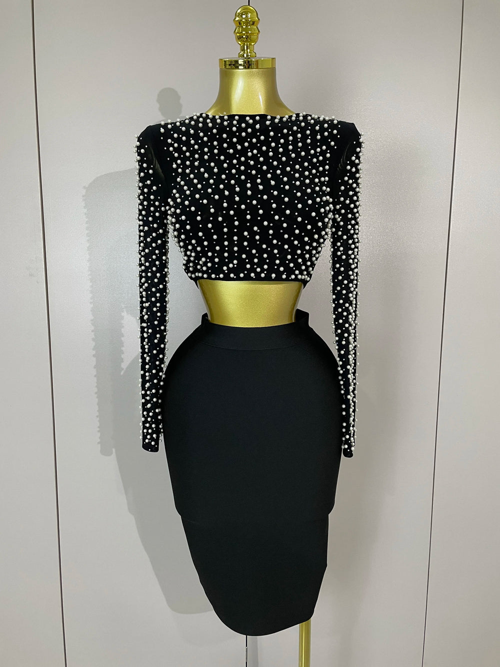 Black dress set with pearl embellishments on a mannequin against a white background