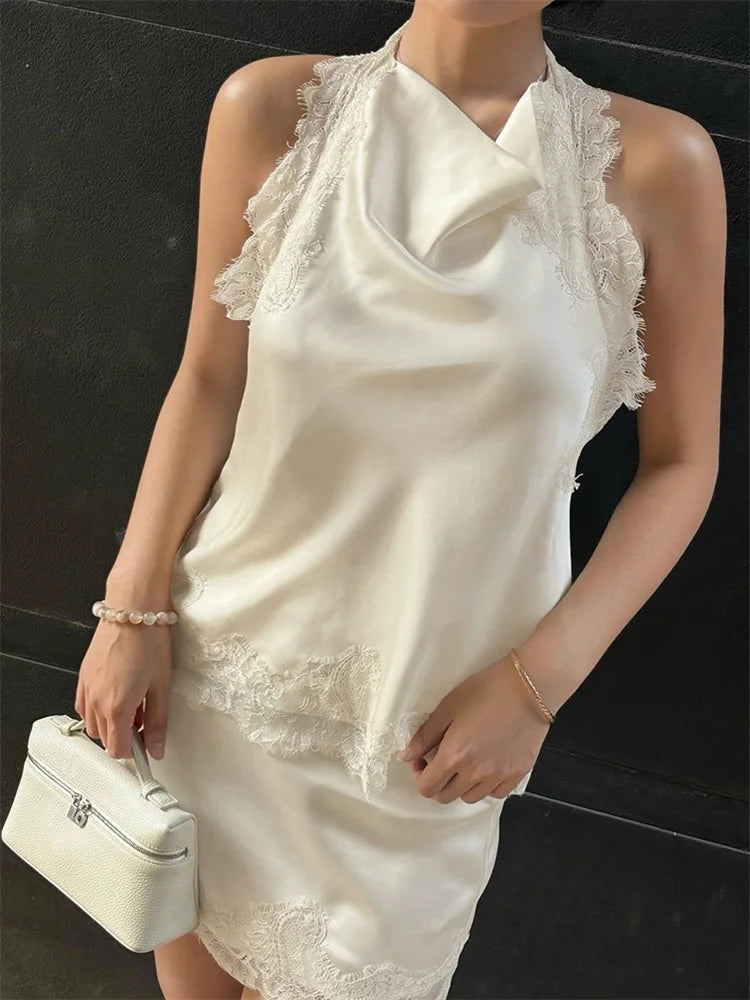 Woman wearing a white lace dress holding a matching handbag against a black background