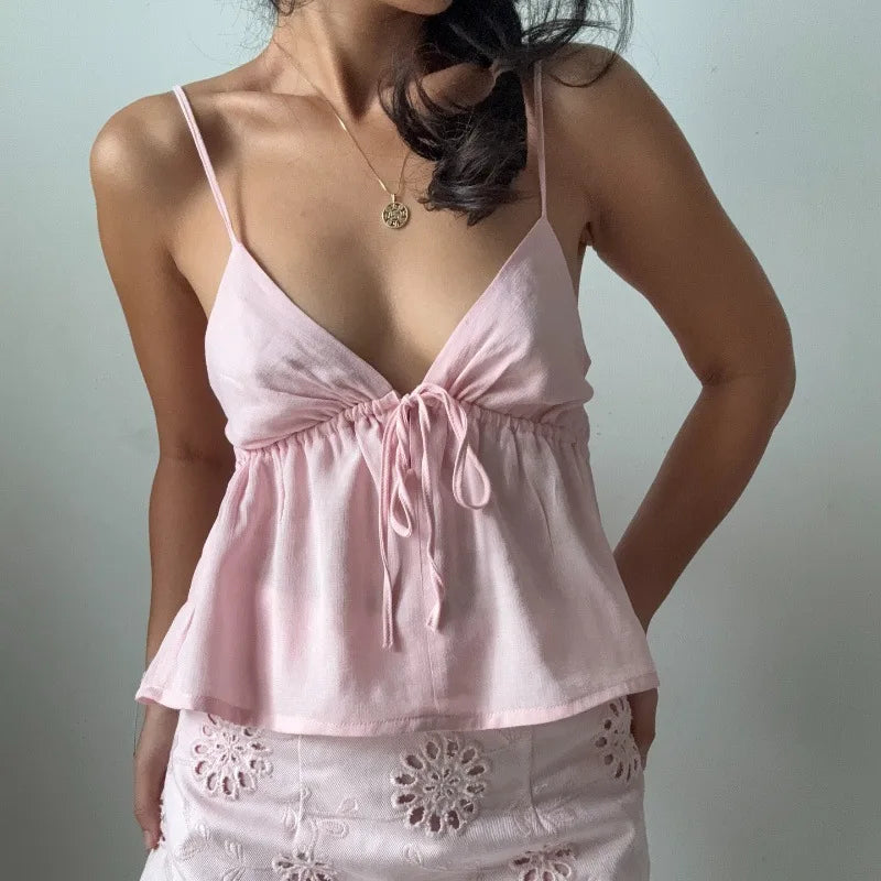 Woman wearing a pink top with thin straps and a white skirt with floral patterns against a plain background