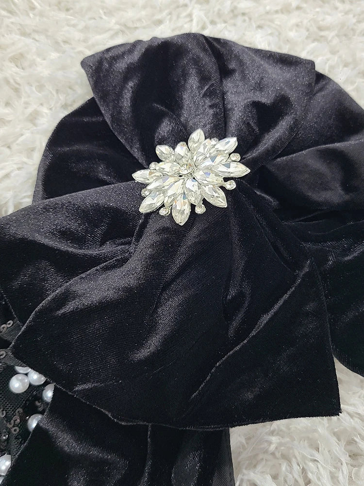 Black satin headband with a decorative pearl flower on a textured white background