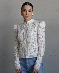 Woman wearing a white lace blouse with long sleeves against a gray background